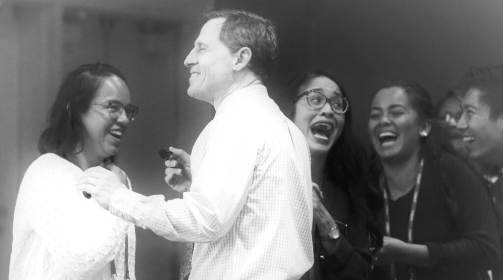 A diverse group of professionals laughing together as Chris Scappatura sparks genuine connection and contagious enthusiasm during an interactive learning experience.